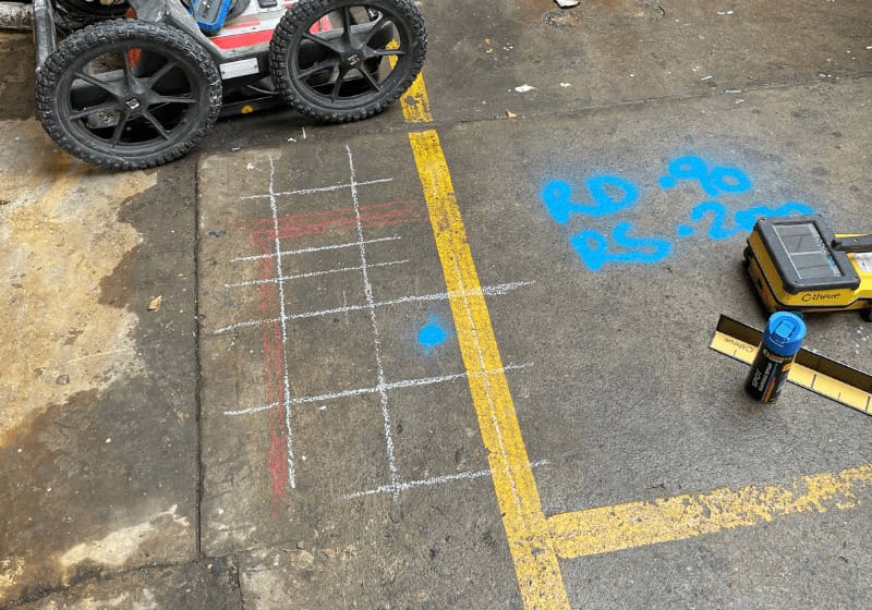 Concrete x-ray vs GPR: chalk scan grid and spray-painted notes on a concrete slab beside a GPR scanner